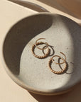 14k gold fill Spiral Twists laid on a gray plate in the sunlight. These earrings are perfect foe everyday wear. These hoop earrings give the allusion that you have two earrings in at once. when all you need is one ear hole. - Token Jewelry