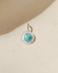 sterling silver round charm with turquoise gemstone on a light dish
