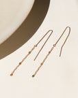 A 14k gold fill threader displayed on a cream backdrop in the sunlight