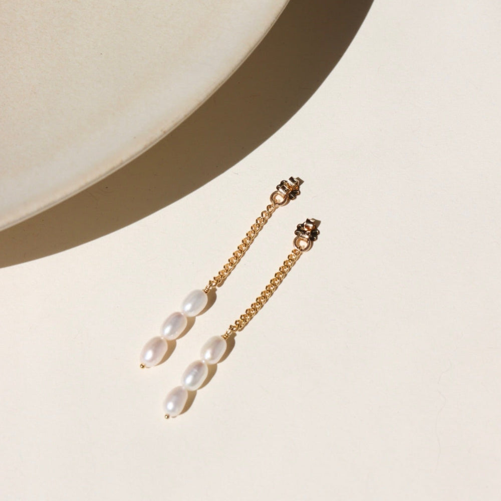 A 14k gold fill curb chain backdrop with three trillium pearls at the bottom of each chain, the backdrops are displayed on a cream display in the sunlight
