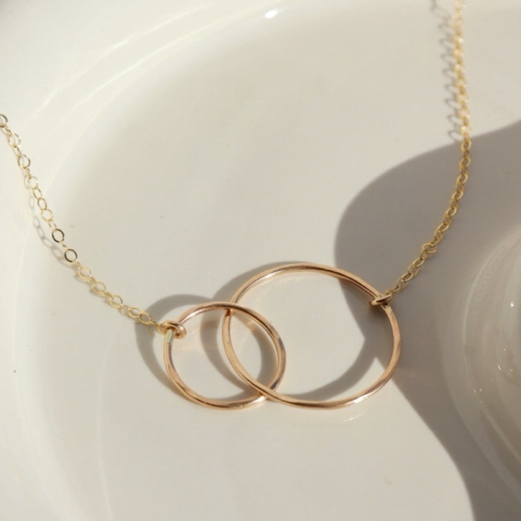 14k gold fill Unity Necklace laid on a white plate in the sunlight.
