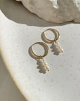 14k gold fill Petite Pearl Hoops laid on a white plate in the sunlight. These earrings feature a Goldie hoop with three tiny gemstone studs. - Token Jewelry