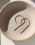 14k gold fill nine earrings laid on a gray plate in the sunlight. These earring give the effect of the number 9. 