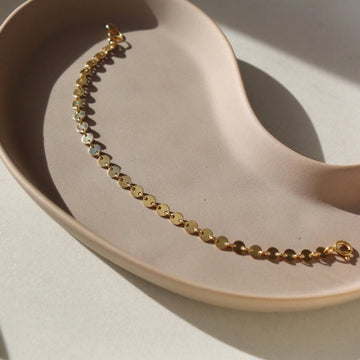 14k gold fill Starlight Bracelet placed on a tan plate in the sunlight. This bracelet features a circle like disc linked together to create a pretty sparkle effect.