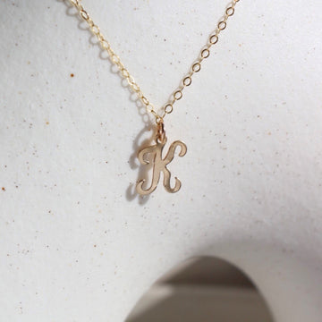 14k gold fill Initial Script Necklace placed on a white pot in the sunlight.