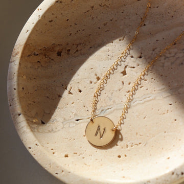 Cream colored plate with a 14k gold fill necklace laid across featuring a circle pendent with initial anchored in the middle with the simple chain. Anchored Monogram Necklace - Token Jewelry