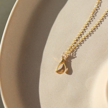 14k gold fill Wishbone Necklace laid on a tan plate in the sunlight.