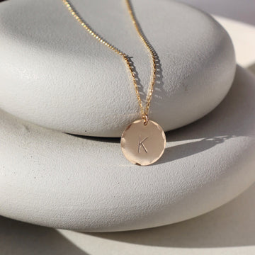 14k gold fill Monogram Coin Necklace placed on a gray dish in the sunlight.