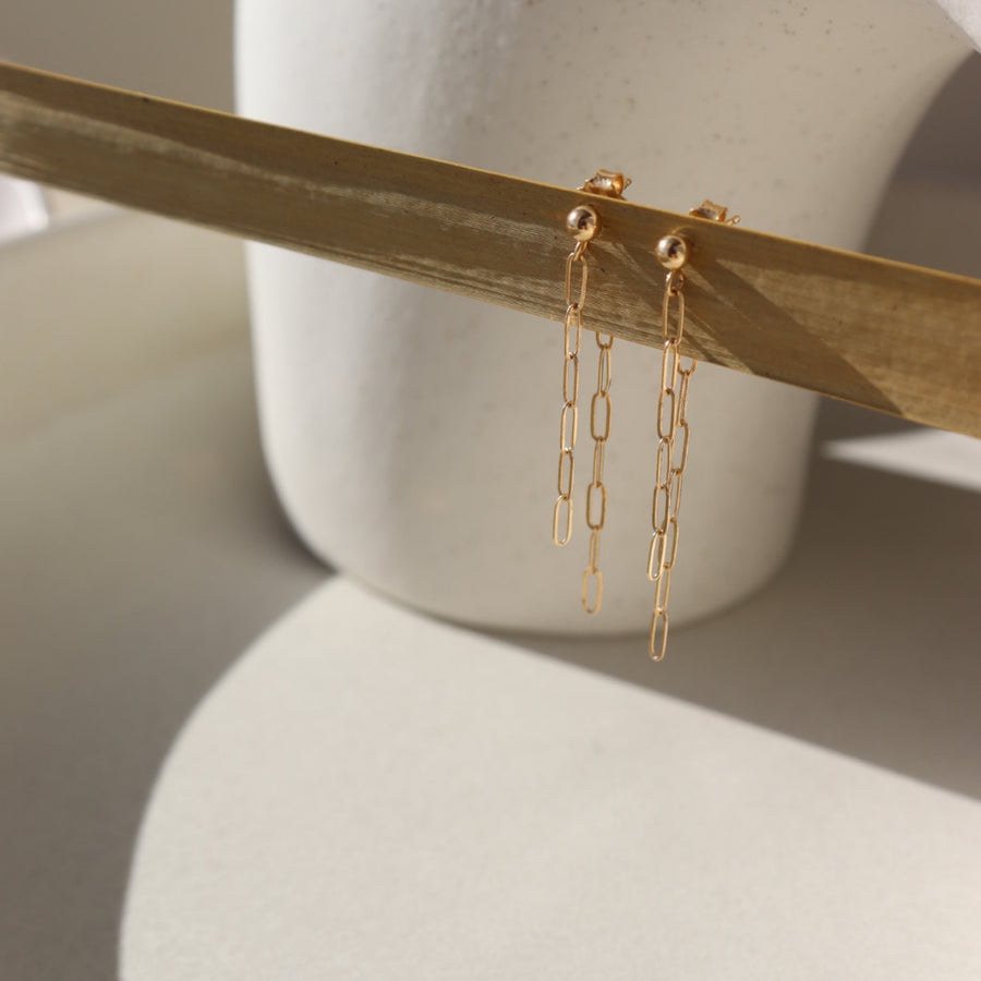 Cosette Double Drop Earrings in 14k Gold laid on a tan plate in the sunlight.