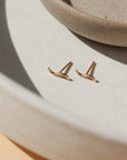 14k gold fill Swell Studs laid on a white plate in the sunlight. These earring are a perfect stud to layer with your other token earrings. This earring give the allusion  of a little "s".