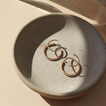 14k gold fill Spiral Twists laid on a gray plate in the sunlight. These earrings are perfect foe everyday wear. These hoop earrings give the allusion that you have two earrings in at once. when all you need is one ear hole.  - Token Jewelry
