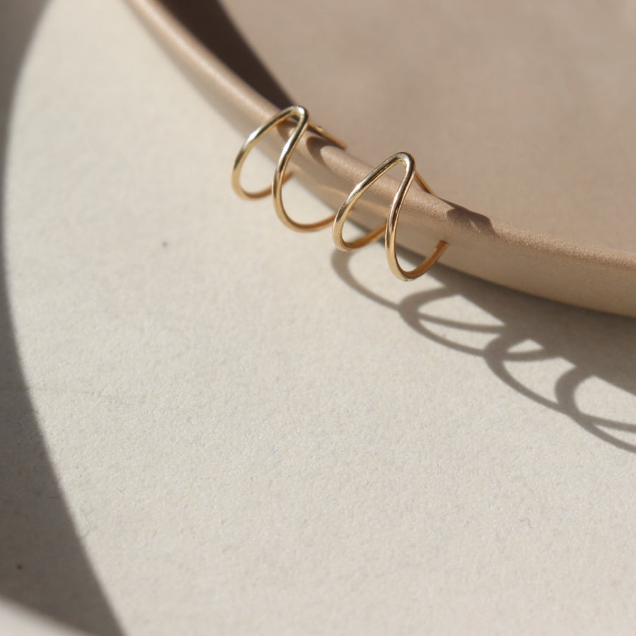 14k gold fill wishbone studs laid on a tan plate in the sunlight.