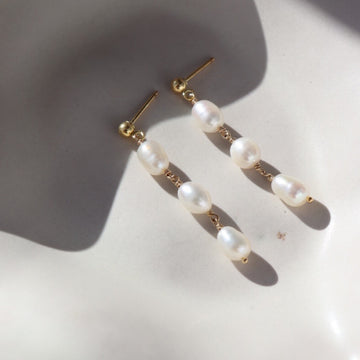14k gold fill Trillium Pearl Drop earring laid on a white plate in he sunlight. These earrings a perfect stud earring that gives the dangle look. 