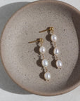 14k gold fill Trillium Pearl Drop Earrings laid on a gray plate. These earrings a perfect stud earring that gives the dangle look.