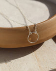 925 Sterling Silver Eternity Necklace placed on a cream colored dish. This necklace and plate is sitting in the sunlight. This necklace features an open circle disc that is attached to our simple chain. Token Jewelry is hypoallergenic and nickel free. - Token Jewelry