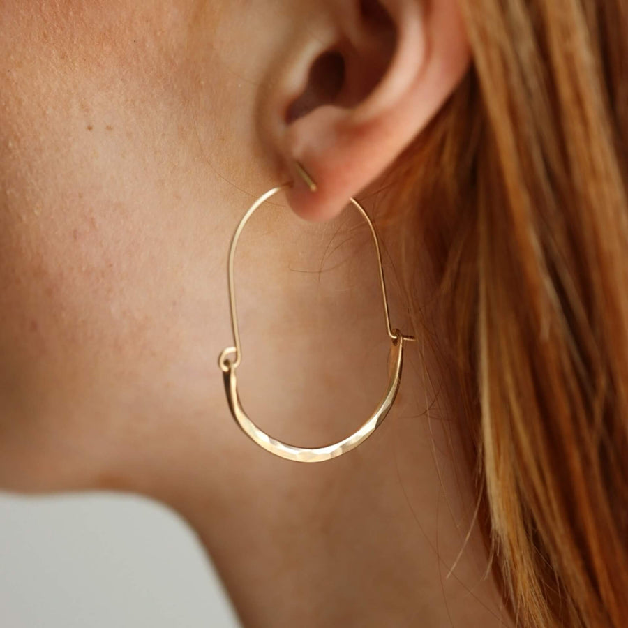 Model wearing Hammered Paloma Hoops. These earrings feature a wire around 1/2 inch shaped like an oval, then followed by the other half of the oval that is hammered.