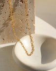 14k gold fill Stevie Chain laid in the sunlight on a white plate. This chain features a twisted loop look. Delicate but makes a perfect stack to layer with your other token jewelry pieces.