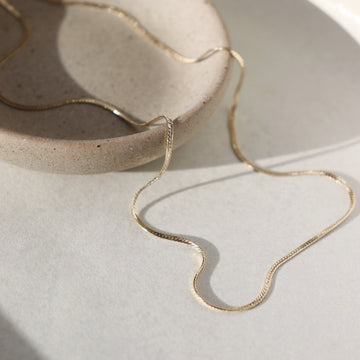 14k gold fill Skinny Herringbone Chain laid on a white paper on a gray jewelry plate. This necklace is perfect for everyday.
