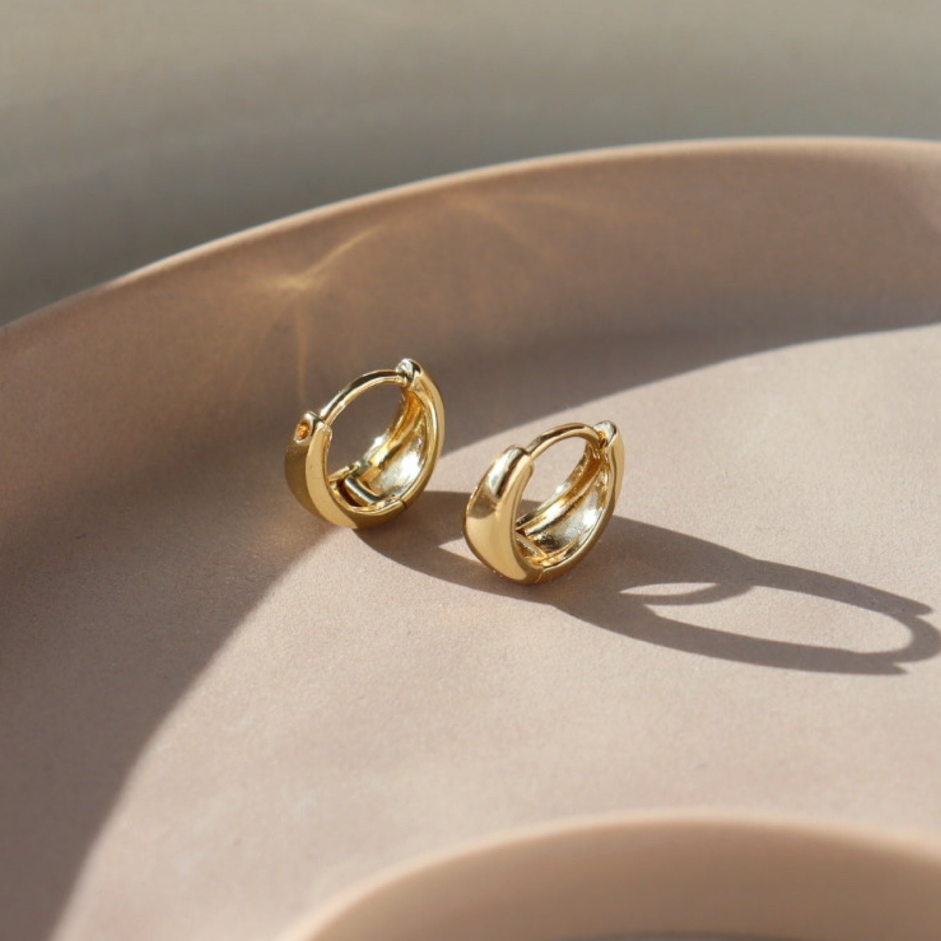 Small Gold Huggie Hoops sitting on a jewelry tray