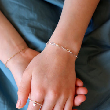 Photo of a young girl's wrist who is wearing various 925 sterling silver jewelry made by Token Jewelry, including a delicate Clara Chain