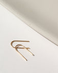 14k solid gold wire formed into arch shaped earrings with one hammered end, photographed on a white table next to a white dish