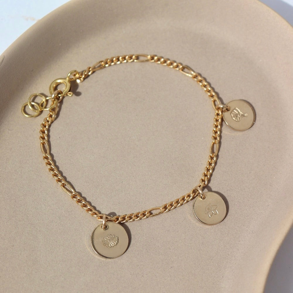 14k gold fill Birth Flower Charm Bracelet laid on a tan plate in the sunlight. This Bracelet feature the Demi Alexandra chain with as many birth flower charms as you want.