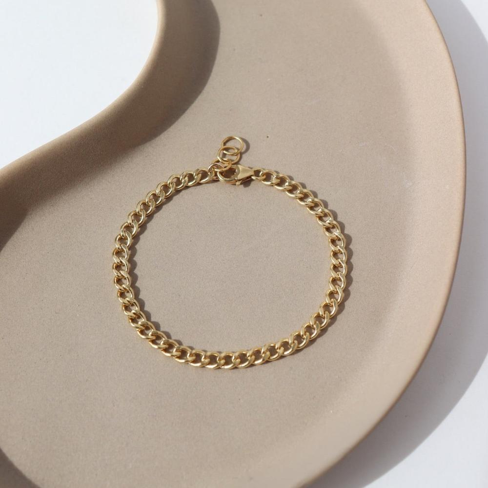 14k gold fill Demi Alexandra Bracelet laid on a tan plate in the sunlight.