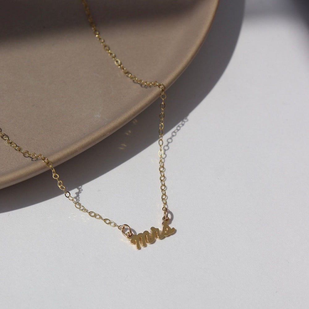 14k gold fill  Mrs.Necklace laid on a white jewelry dish in the sunlight. This is perfect to gift any bride to be in your life.