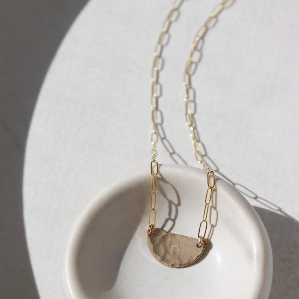 14k gold fill necklace Laid on a white pot. This necklace features a half circle hammered in the middle each side connected by the cosset chain.