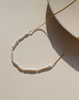 14k gold fill Maren Pearl Necklace laid on a tan plate in the sunlight.