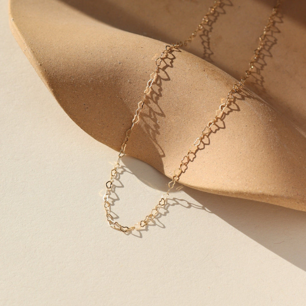 14k gold fill Petite heart chain from Token Jewelry, photographed on a tan, organically shaped dish. This chain features a gold tiny heart wire throughout the whole chain. 