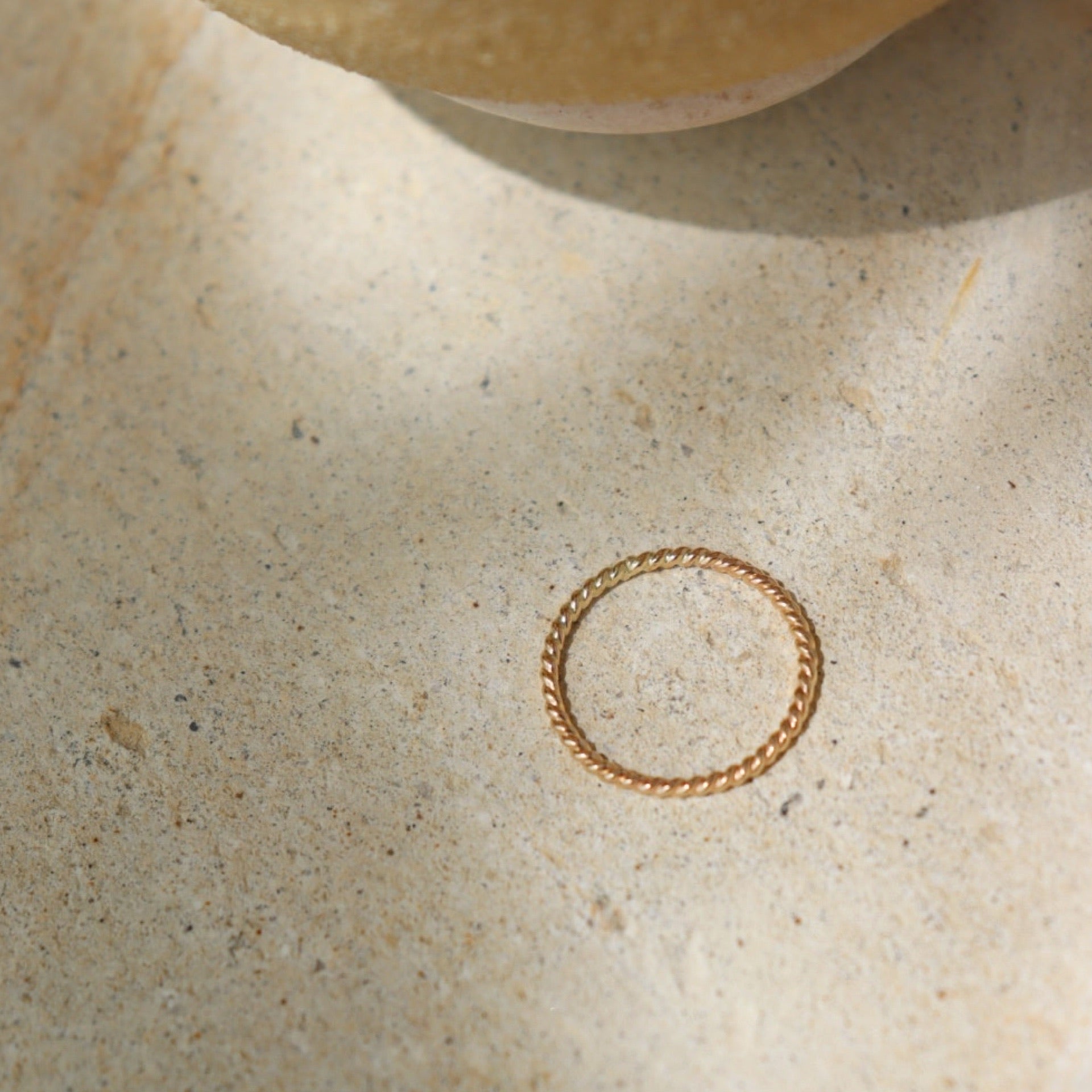 14k gold fill Spiral Midi Ring laid on a tan plate in the sunlight. This ring band features a spiral look and is perfect for stacking.
