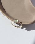 14k gold fill Sweet Pea ring laid on a tan plate in the sunlight. This Ring features a smooth band with a prehnite gemstone.