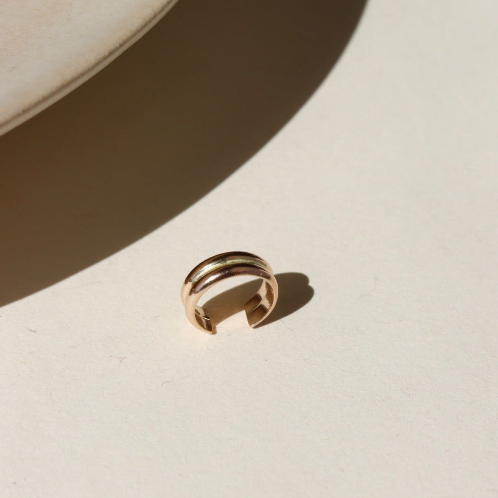 A 14k gold fill double layered ear cuff, displayed on a cream back drop in the sunlight 