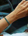 Model wearing the 14k Gold Fill Sunburst Bracelet, a delicate gold chain bracelet layered with chrysocolla gemstone bracelets and styled with gold rings in a lifestyle setting.