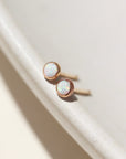 14k gold fill Petite opal studs laid on a tan plate in the sunlight. these earring feature a 3mm opal gemstone followed by a bezel ear post.