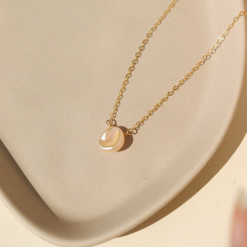 14k gold fill freshwater pearl necklace laid on a peach colored plate. This necklace features the simple chain with the freshwater pearl wired in the middle.