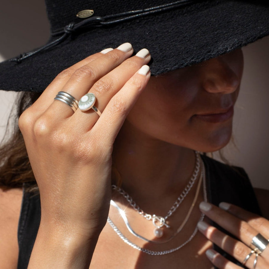 925 Sterling Silver Trinity ring spirals into three bands, photographed on a model wearing all silver jewelry and a black cowboy hat. This ring features the look of the three layered band look but its only one ring.