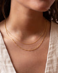 a 14k gold fill necklace made up of two chains, photographed on a model wearing an off white linen vest