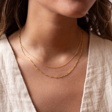 a 14k gold fill necklace made up of two chains, photographed on a model wearing an off white linen vest
