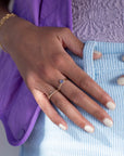 Model wearing 14k gold fill Tanzanite Ring. This ring features a simple smooth band featuring a Tanzanite cab. The model is also wearing other 14k gold fill bands, light blue corduroy shorts, a lavender purple textured top, and a purple vest
