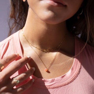 Model Wearing Cherry Blossom Necklace in 14k gold fill. This Necklace features a simple chain with a dangle gemstone. The gemstone that is featured in this necklace is the Cherry Agate Sphere. 