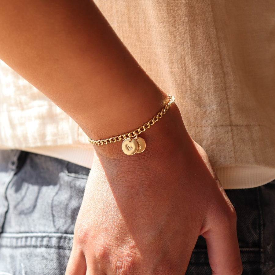 14k gold fill bold link chain Demi Alexandra Bracelet featuring two gold fill disks with a heart and an "S", worn by a model wearing black jeans and a cream top