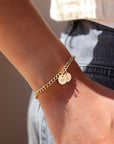 14k gold fill bold link chain Demi Alexandra Bracelet featuring two gold fill disks with a heart and an "S", worn by a model wearing black jeans and a white top