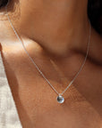 a sterling silver necklace featuring a dainty chain and a small, concave, polished disc, photographed on a model wearing a cream colored linen vest