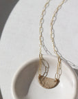 14k gold fill necklace Laid on a white pot. This necklace features a half circle hammered in the middle each side connected by the cosset chain.
