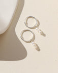 Silver petite hoops featuring three mini pearls hanging from each hoop. Earrings are displayed on cream backdrop. 