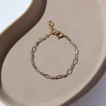 14k gold fill Tiny Clara Bracelet laid on a tan plate. This bracelet is made for children making it so that you and a child you know can match.