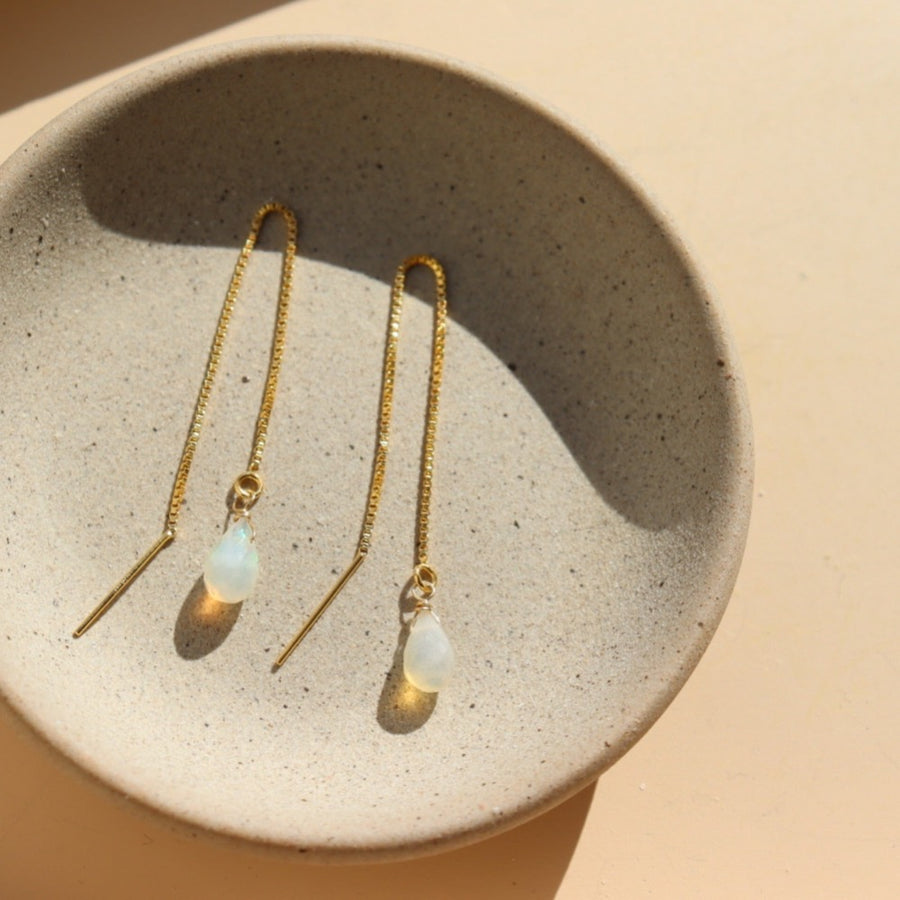 Handmade teardrop shaped faceted opals connected to a delicate box chain threader earring chain and draped over a jewelry tray in the sunlight