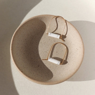 14k gold fill Howlite arches laid on a gray plate. These earrings feature a white Howlite stone and a arch type wire earring.  